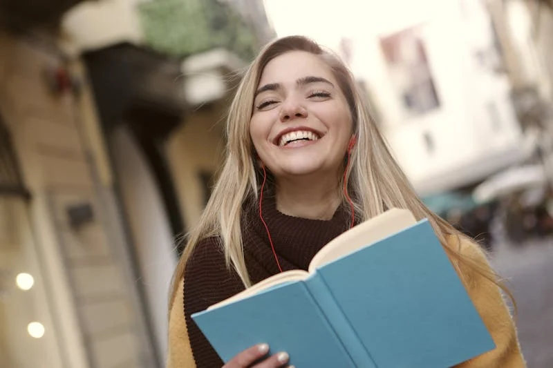 Fotografía de una joven estudiante riendo muy contenta con sus libros