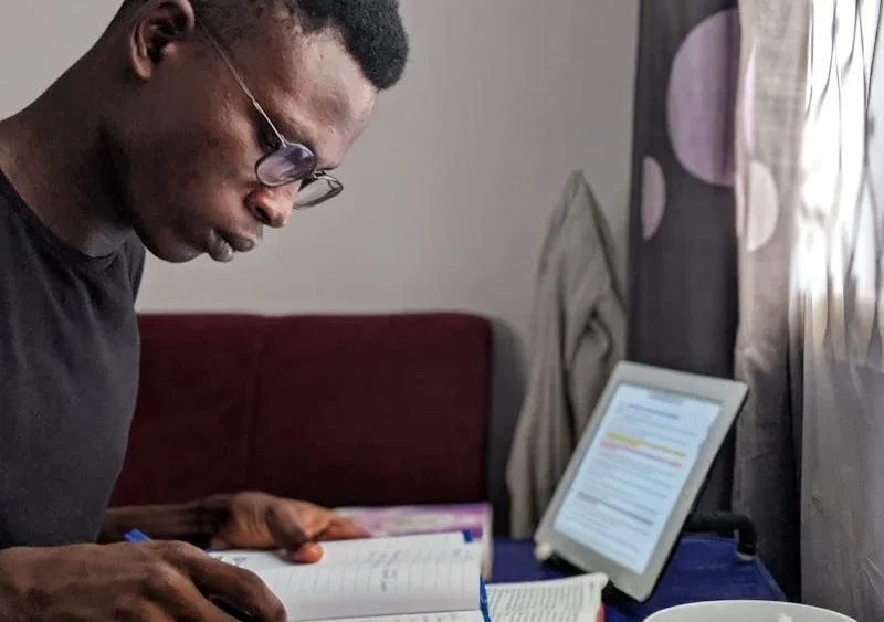 Fotografía de un hombre de raza negra estudiando un libro en su cuarto.