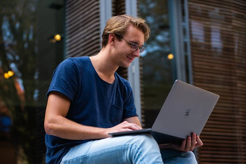 Fotografia de un joven sonriendo y estudiando en su laptop