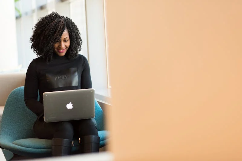 Fotografía de una muchacha sentada en un sillón mirando y estudiando en su laptop
